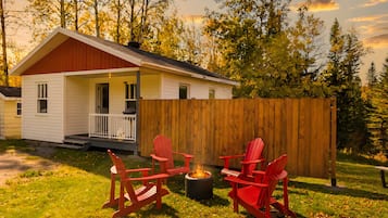 A small house with a porch, a fire pit, and red Adirondack chairs.