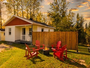 Une petite maison avec une véranda, un foyer et des fauteuils Adirondack rouges.
