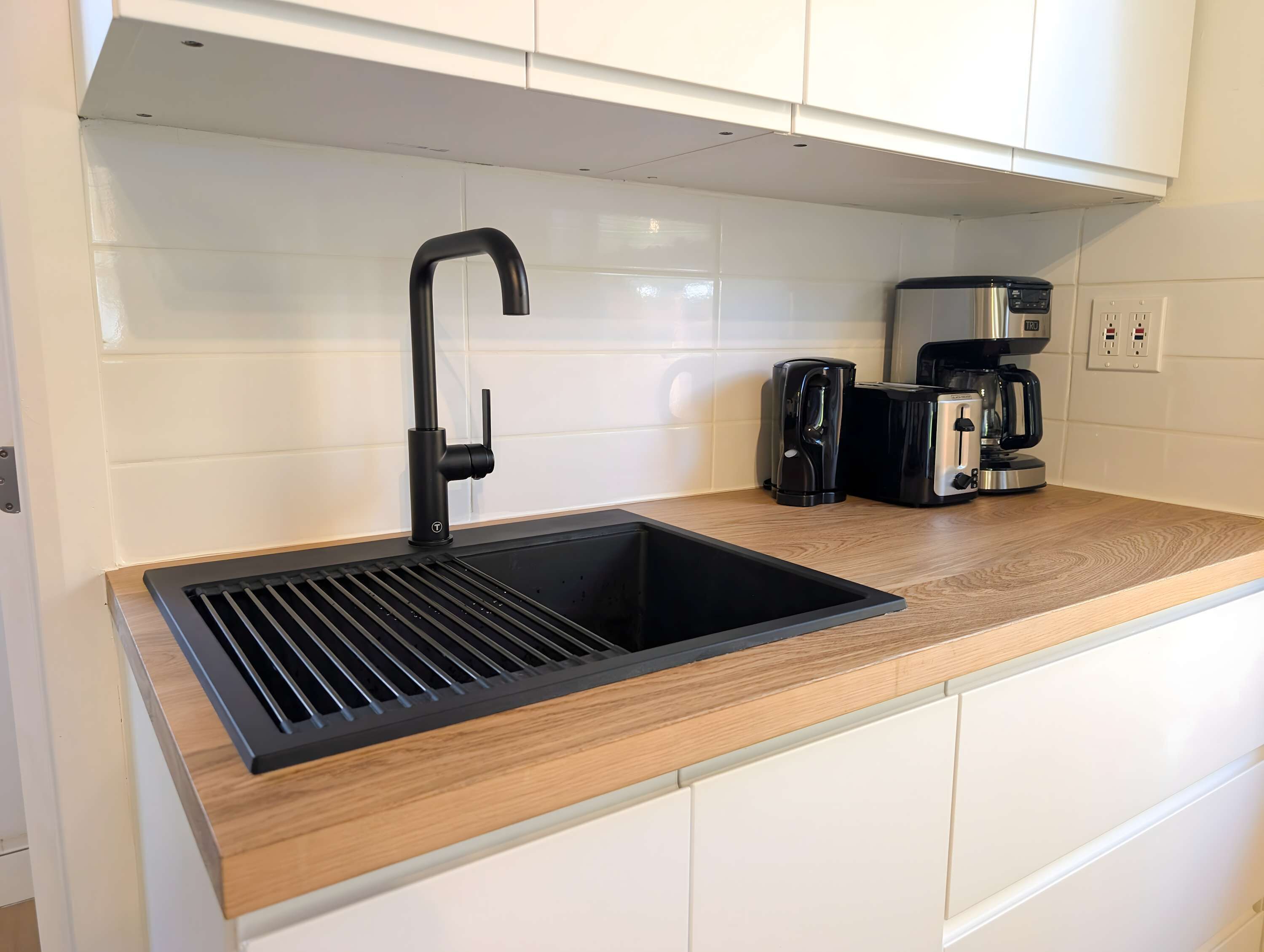 Eine Küche mit einem schwarzen Spülbecken, einer Kaffeemaschine und einem Toaster auf der Arbeitsfläche.