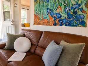 Un canapé en cuir marron agrémenté de plusieurs coussins, un livre posé dessus, et un grand tableau floral accroché au mur.