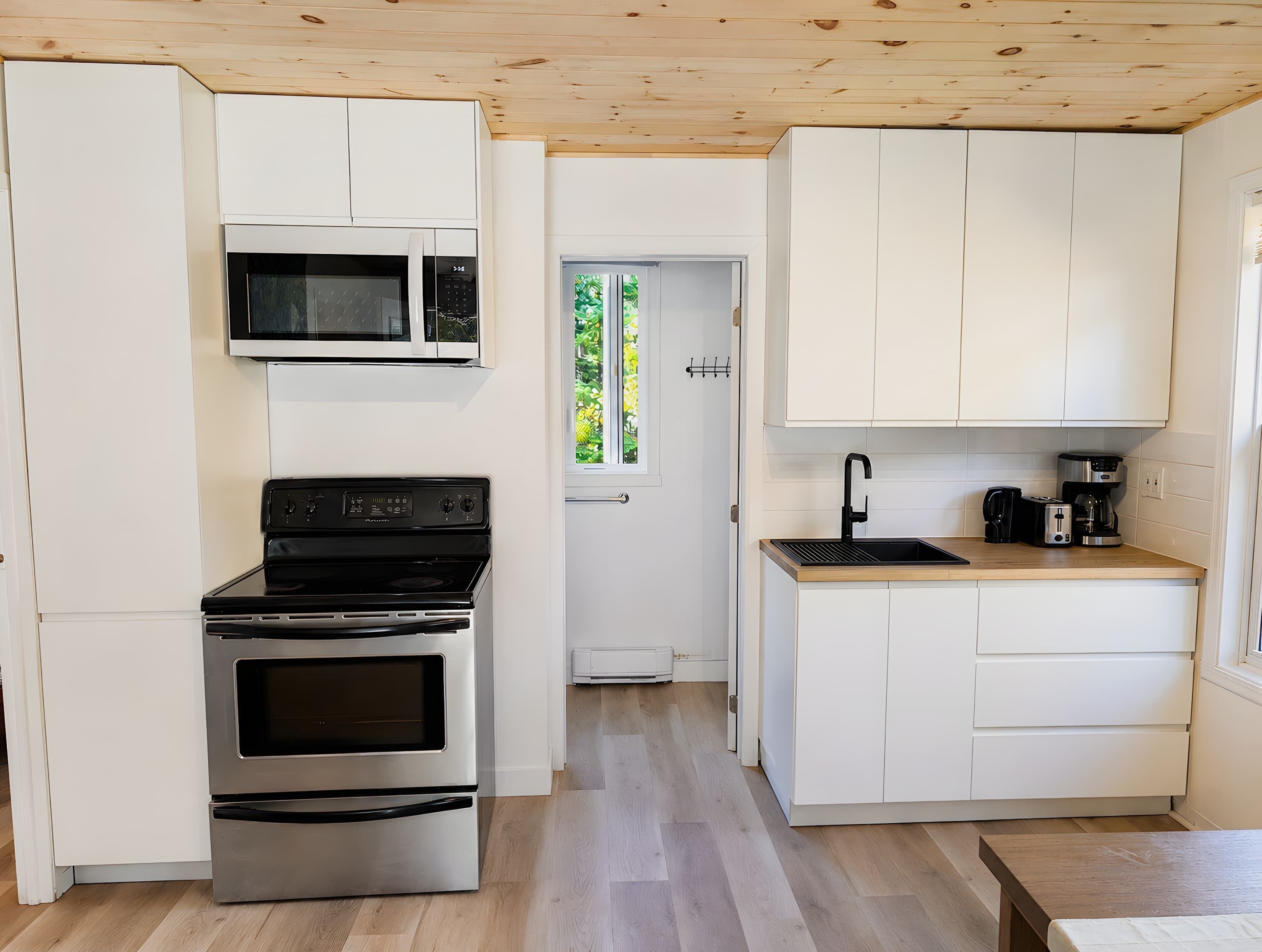 A compact kitchen with white cabinetry, a built-in microwave, a stainless steel oven, and a wooden countertop with a coffee maker.