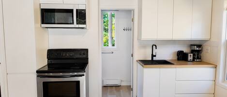 Una cocina funcional con armarios blancos, microondas integrado, horno de acero inoxidable y encimera de madera con cafetera.