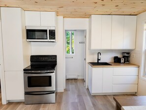 Une cuisine compacte avec des meubles blancs, un four à micro-ondes encastré, un four en acier inoxydable et un plan de travail en bois sur lequel se trouve une machine à café.