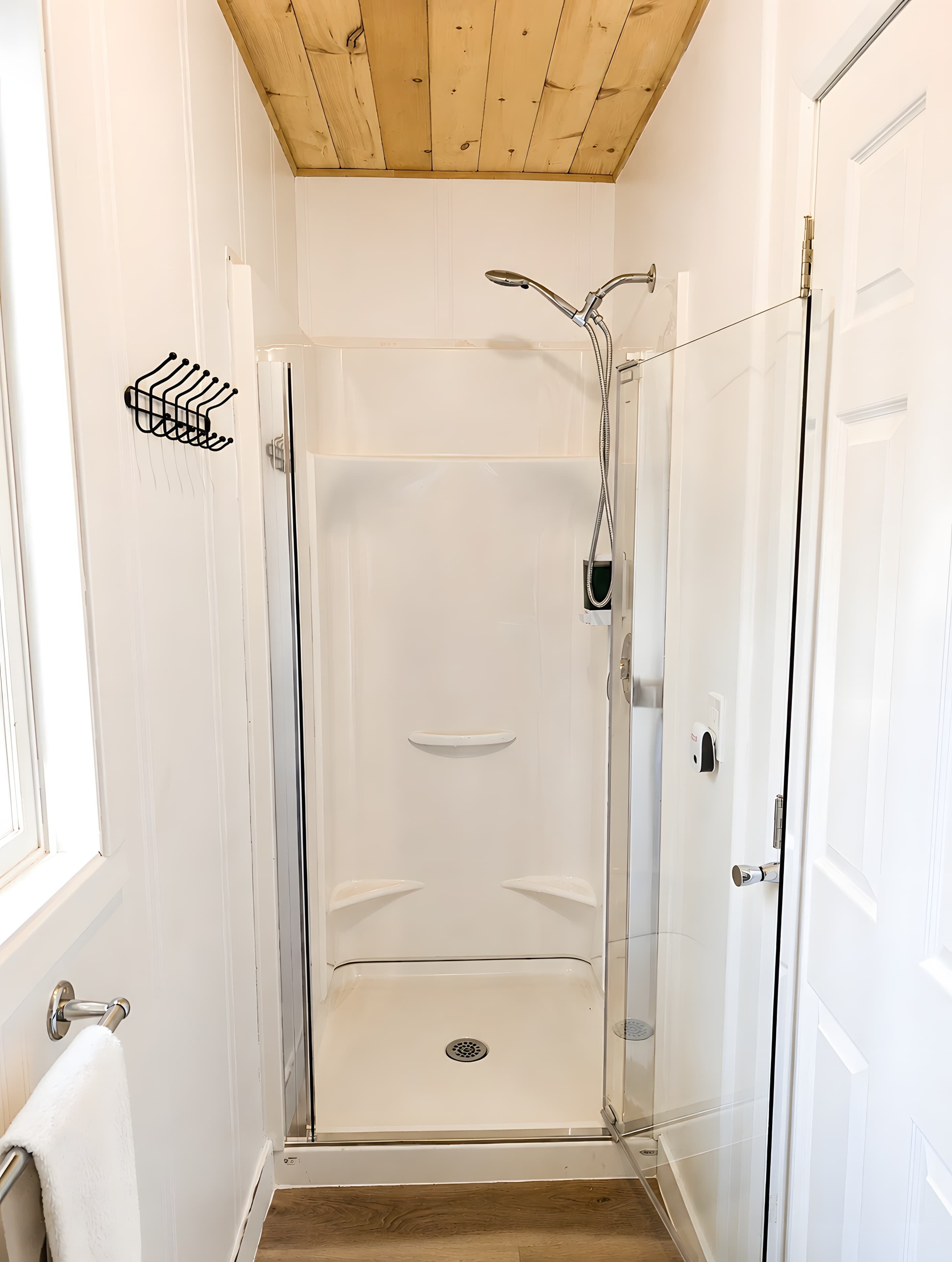 Una doccia a pavimento con porta in vetro, soffitto in legno e parete bianca.