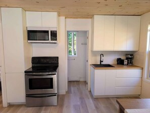 Eine kleine Küche mit Mikrowelle, Backofen und Spüle, Holzboden und weißen Schränken.