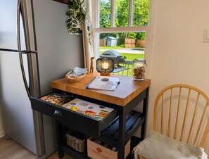 Une cuisine avec une table en bois, un réfrigérateur, un panier en osier, un bocal de biscuits et une fenêtre donnant sur l’extérieur.