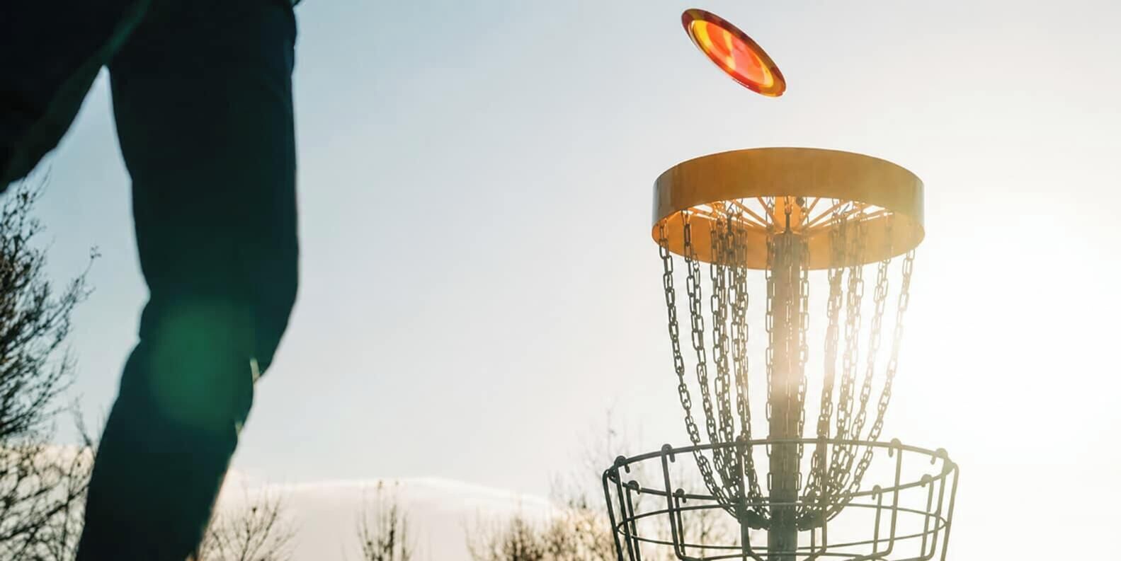 Una canasta de disc golf con cadenas y un disco en pleno vuelo.