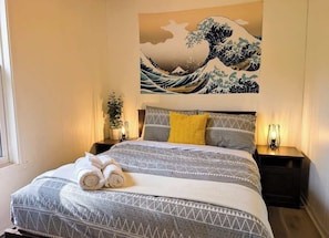 Ein Hotelzimmer mit einem Bett, einem Wandbild, zwei Nachttischen und einem Fenster.