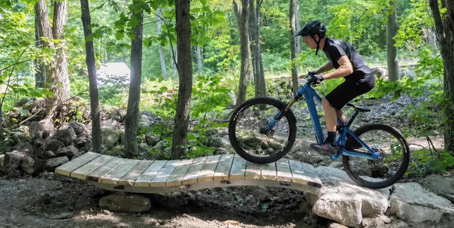 Una persona in sella a una mountain bike su un ponte di legno in una zona boschiva.