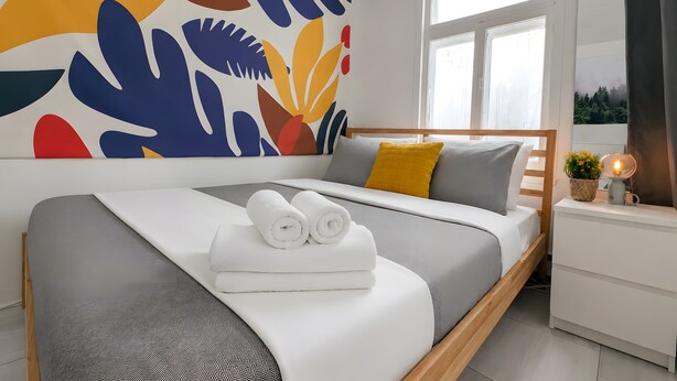 Una camera da letto moderna con un letto, una parete con arte astratta, una finestra e un comodino con una lampada.