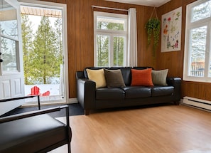 Ein Zimmer mit einer schwarzen Ledersofa, Holzwänden und großen Fenstern.