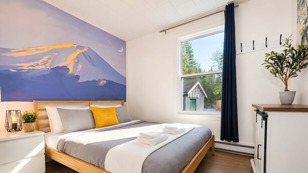 A modern bedroom with a wooden bed, a large painting, a window with curtains, and a potted plant. - Hot Tub Chalet in Charlevoix - Firepit & BBQ (Saint-Tite des Caps)