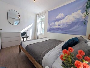 Een slaapkamer met een bed, een stoel, een bureau, een spiegel en een muur met een schilderij.