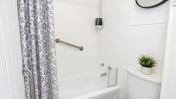 Et badeværelse med bruser, toilet og en lille potteplante.