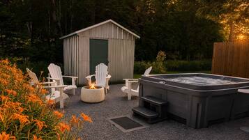Ett bubbelbad, vita Adirondack-stolar och ett förråd i en trädgårdsmiljö.