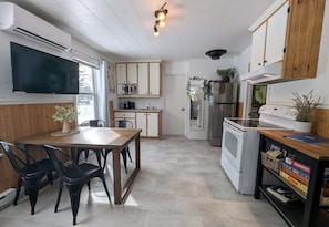 A modern kitchen with a dining table, chairs, a TV, cabinets, a microwave, a refrigerator, and a washing machine. - Charlevoix - Chalet w/ Spa, BBQ, Firepit & Nature (Saint-Tite-des-Caps)