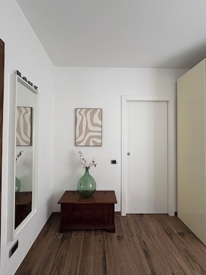 Un couloir doté d’un plancher en bois, d’un miroir, d’un vase rempli de fleurs et de deux tableaux abstraits accrochés au mur.