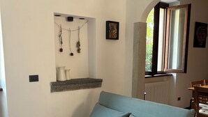 Ein hellblaues Sofa in einem Raum mit Fliesenboden, eine kleine Ablage mit Dekoration, ein Fenster mit Blick und ein Essbereich im Hintergrund.