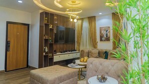 Una sala de estar moderna con sofá, reposapiés, televisor, mueble de entretenimiento e iluminación circular en el techo.