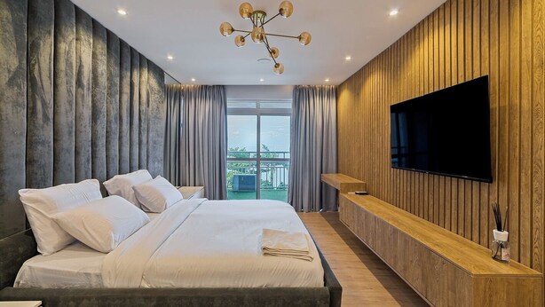 Una habitación de hotel moderna con una cama grande, un televisor, una pared de acento de madera y un balcón con vistas.