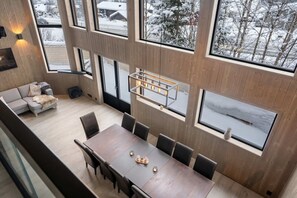 Ein modernes Interieur mit Essbereich, einer Couch und großen Fenstern mit Blick auf eine verschneite Landschaft.