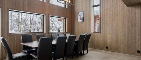 A dining area with a wooden interior, large windows, and a modern chandelier.