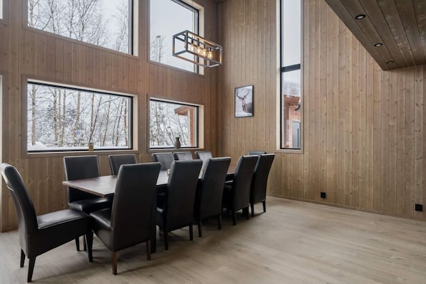 A dining area with a wooden interior, large windows, and a modern chandelier.