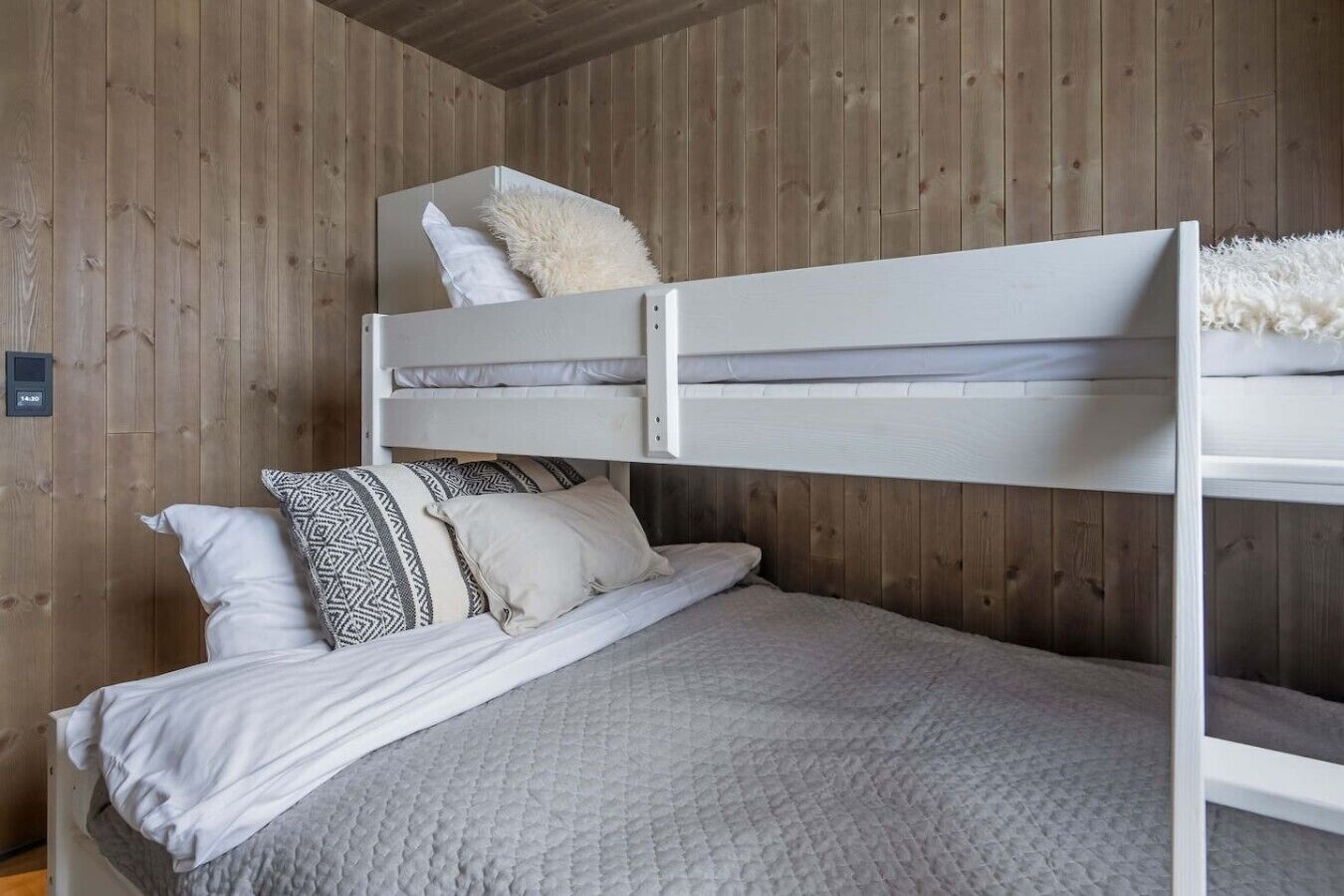 A bunk bed with a white headboard, a lower bed with a quilted blanket, and two pillows with geometric patterns.