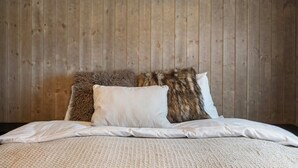 A bed with white bedding and two pillows, one with a fur-like texture, against a wooden paneled wall. - Trysil Ski-in/out Apt, Hot Tub, 4 BR (Trysil)