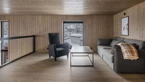 A modern interior with wooden panel walls, a sofa, a chair, a coffee table, and a large window with a view of snow-covered trees. - Trysil Ski-in/out Apt, Hot Tub, 4 BR (Trysil)