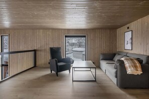 Ein modernes Interieur mit Holzwandverkleidung, einer Couch, einem Sessel, einem Couchtisch und einem großen Fenster mit Blick auf schneebedeckte Bäume.