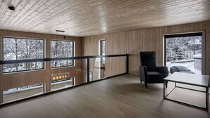 A modern interior with wooden panel walls, large windows, a black chair, and a table. - Trysil Ski-in/out Apt, Hot Tub, 4 BR (Trysil)