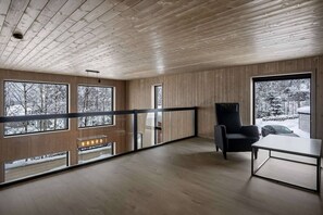 Ein modernes Interieur mit Holzwandverkleidung, großen Fenstern, einem schwarzen Sessel und einem Tisch.