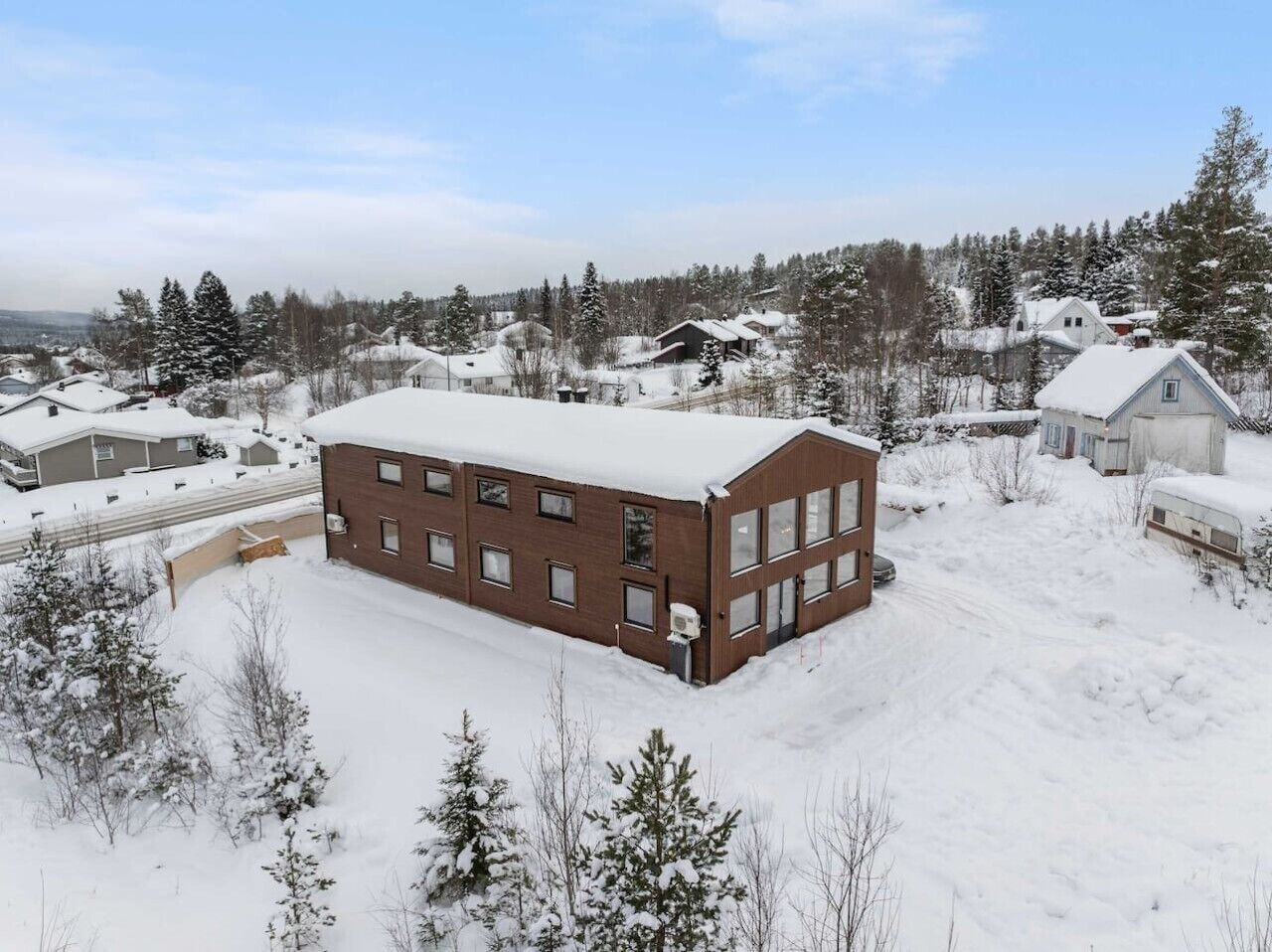 En stor, rektangulär byggnad med många fönster, omgiven av snötäckta träd och hus.