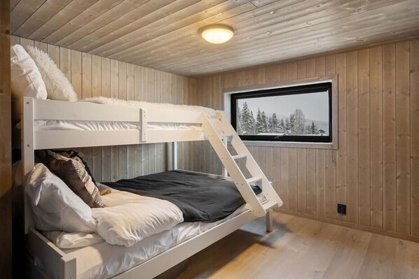 Ein Stockbett mit einer Leiter, ein Fenster mit Blick auf Schnee und Holzwände.