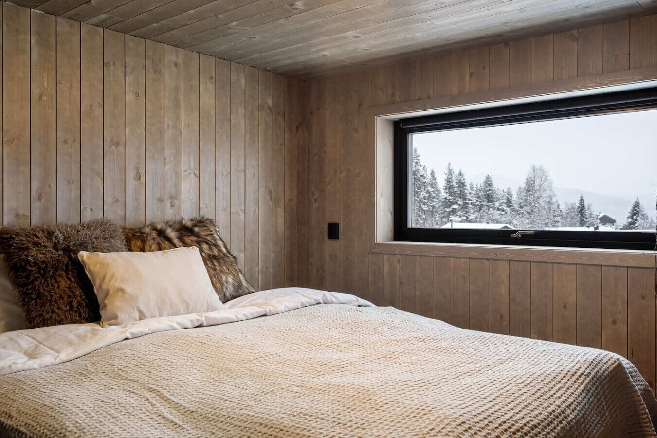 A bedroom with wooden walls, a large window, and a bed with a textured blanket.