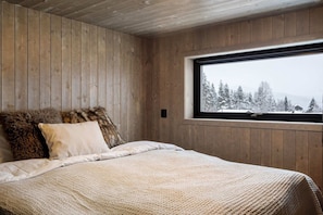 A bedroom with wooden walls, a large window, and a bed with a textured blanket.