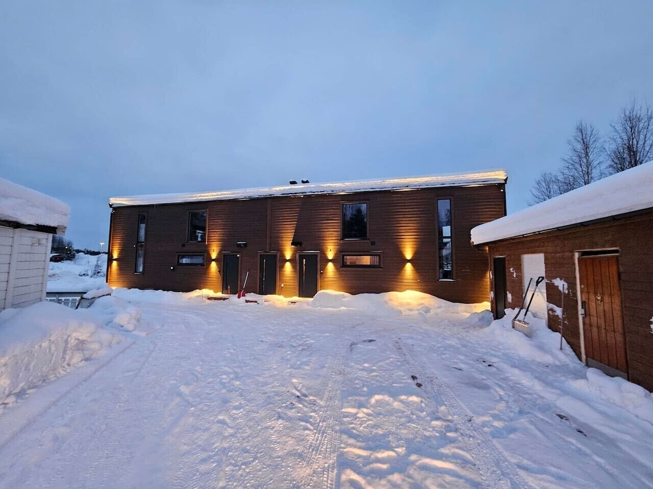 Un bâtiment à deux étages, avec une allée enneigée et un garage en bois.