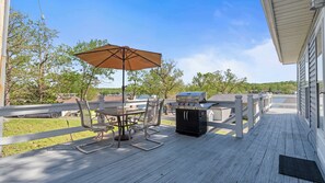 A deck with a grill, chairs, and an umbrella. - Wake & Walk Retreat w/ Hot Tub (Lake Ozark)