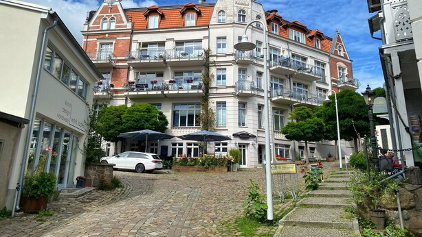 Ein historisches Gebäude mit mehreren Balkonen, einer Kopfsteinpflasterstraße und einem parkenden Auto.