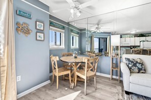 Ein Essbereich mit einem runden Holztisch und Stühlen, einem Deckenventilator und einem durch eine Glastrennwand sichtbaren Küchenbereich.