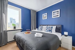 A bedroom with a large bed, a nightstand, a window with curtains, and two framed pictures on the wall. - Lumina apart with parking in Warsaw center (Warszawa)