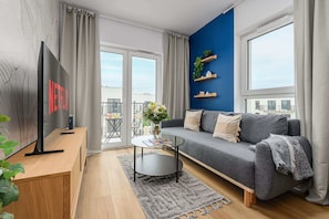 Un salon moderne avec un canapé gris, une table basse, un téléviseur à écran plat et un balcon offrant une vue.