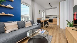 Una sala de estar moderna con un sofá gris, una mesa de centro de vidrio y una cocina al fondo.