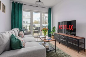 Una sala de estar moderna con sofá, mesa de centro, televisor y puertas corredizas de vidrio que dan a un espacio al aire libre.