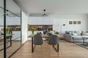 Una cocina moderna con armarios blancos, una mesa de comedor con sillas y un sofá gris en la sala de estar.