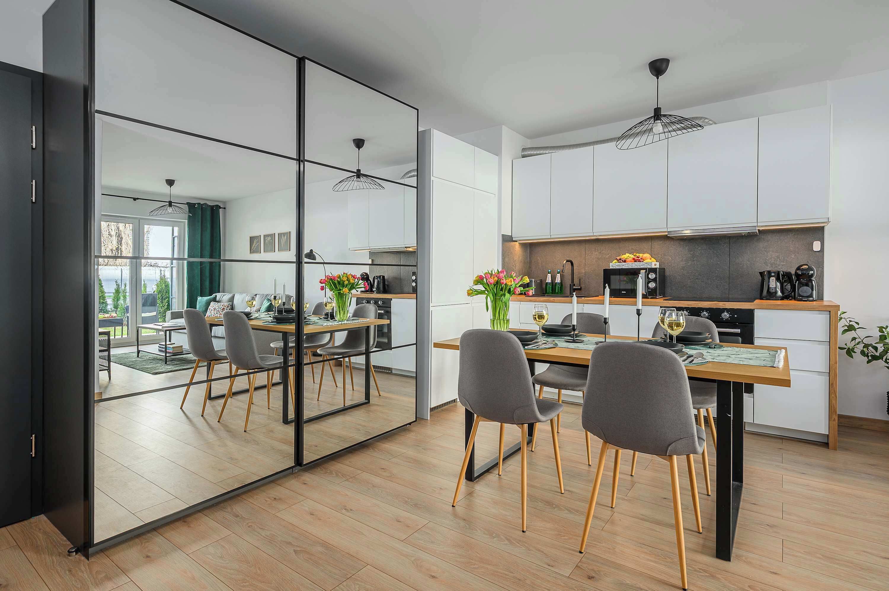 Una cucina moderna con mobili bianchi, un'area pranzo con una parete divisoria in vetro e vista sull'esterno.