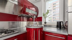 Une cuisine moderne avec des meubles de couleur rouge, des appareils en acier inoxydable et une fenêtre donnant sur un immeuble d’habitation.