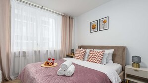 Un lit bien fait, recouvert d’une couverture rose, un plateau avec de la nourriture et des boissons, et deux tableaux encadrés accrochés au mur.