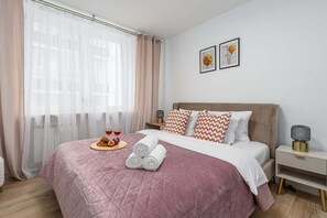 A neatly made bed with a pink quilt, a tray with food and drinks, and two framed pictures on the wall. - Lumina cozy 3-room apart near the city center (Warszawa)